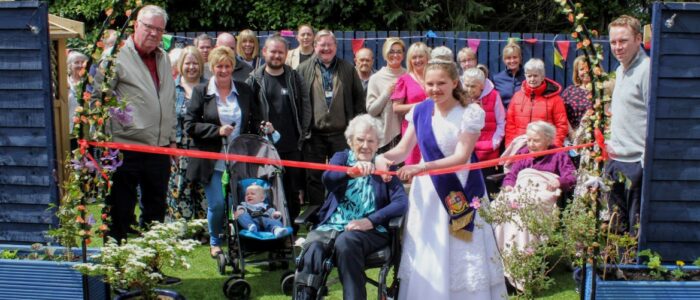 A group photo of Bo'Net community volunteers and current Bo'ness Hospital patient cutting the ribbon on the new garden.