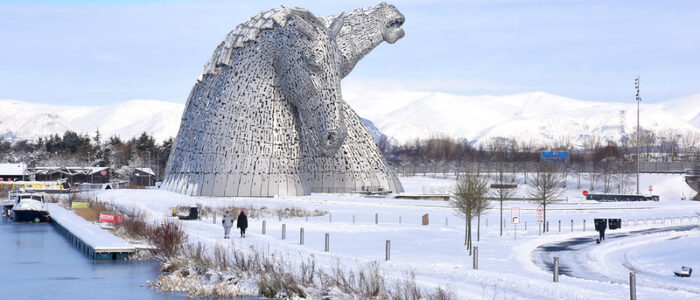 Scenic shot of the Kelpies at Falkirk's Helix, covered in snow. Ochil hills, also dusted in snow, in the background, and the canal in the foreground.